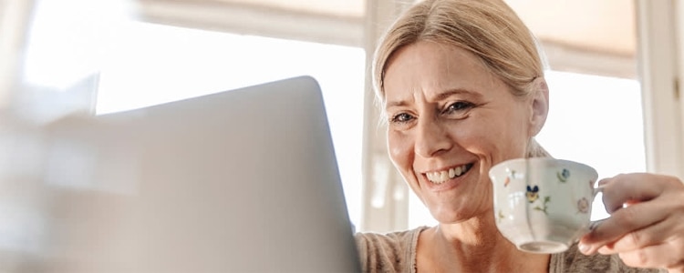 A woman holds a mug as she uses her computer to research and compare high-yield savings accounts and money market accounts.
