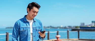 Man smiling at his phone standing near water