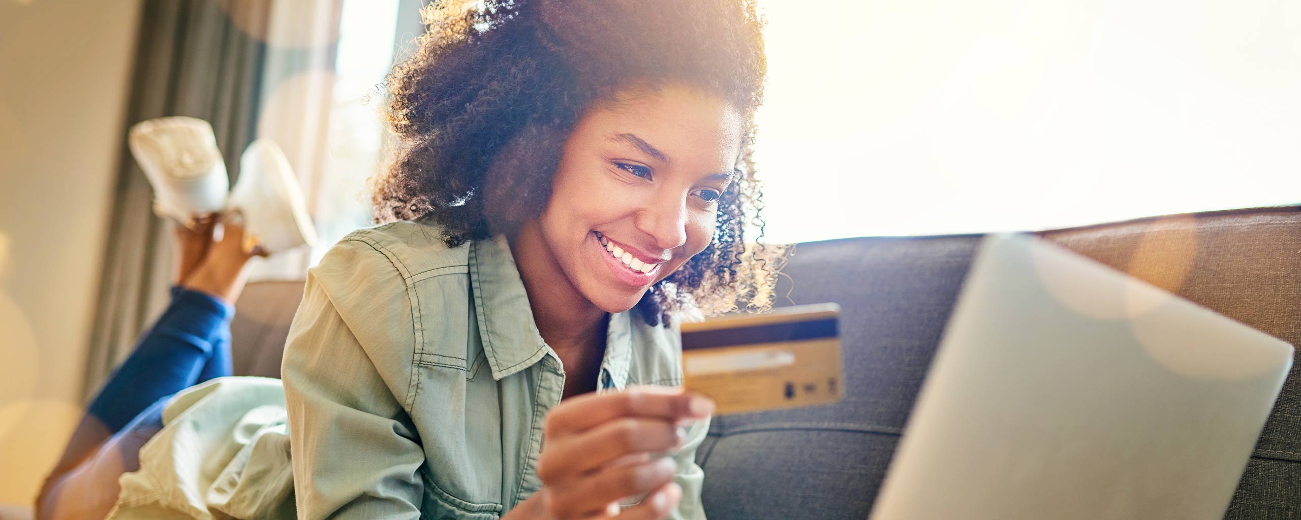 Girl smiles as she holds a debit card and reads through the advantages and disadvantages of a checking account.