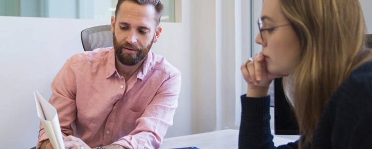 A bearded man and a woman in glasses discuss the benefits of a savings account.