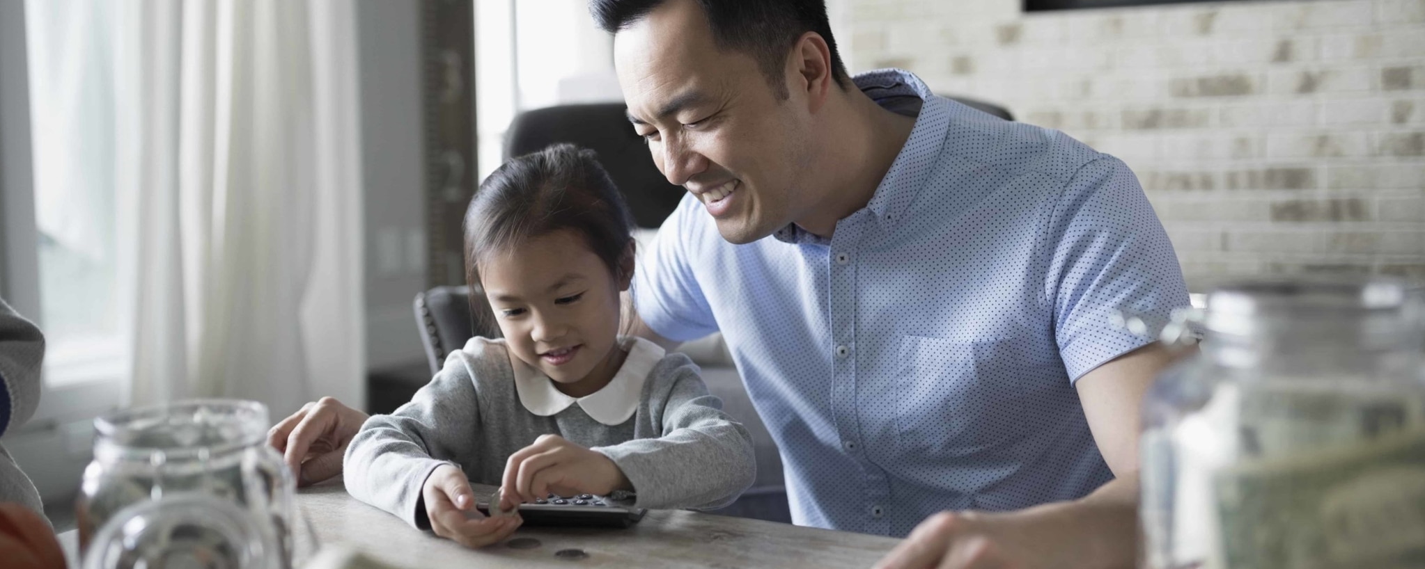 A man and his daughter sit at their kitchen table and count pocket change, which could grow with interest if it were placed in a savings account.