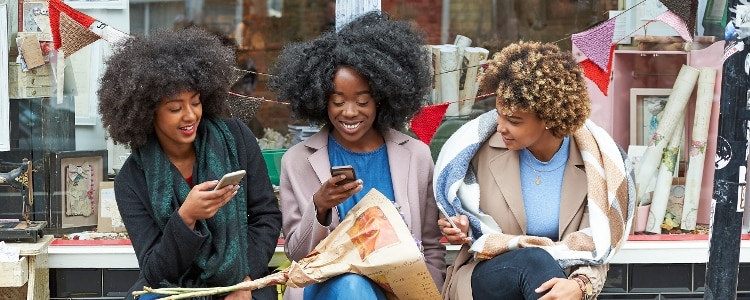 Three women pull out their phones to transfer money to one another’s bank accounts.