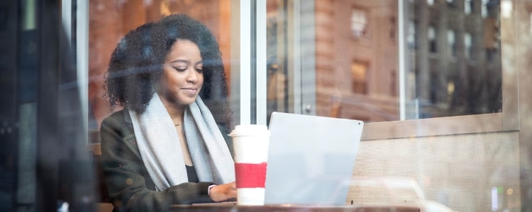 A woman sits at her laptop, a giant cup of coffee in front of her, and safely and securely signs in to her online bank account.