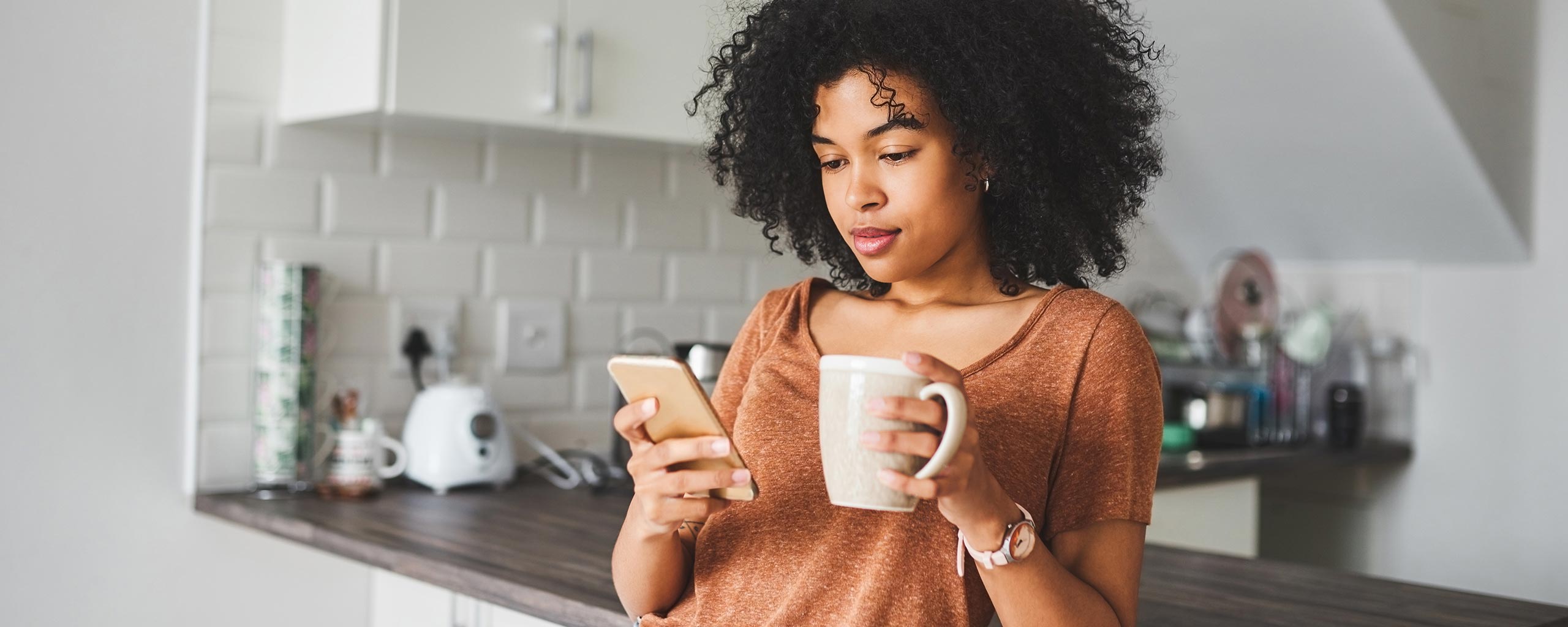 A woman holds her phone and a mug as she considers how to save when interest rates are low.
