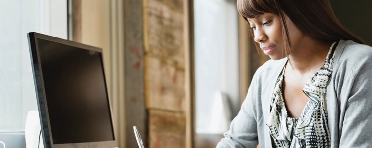 A woman sits at a desktop computer and considers a few questions before opening a savings account.