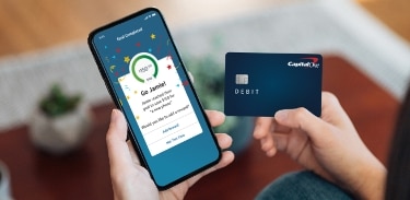 Hands holding mobile phone and Capital One debit card