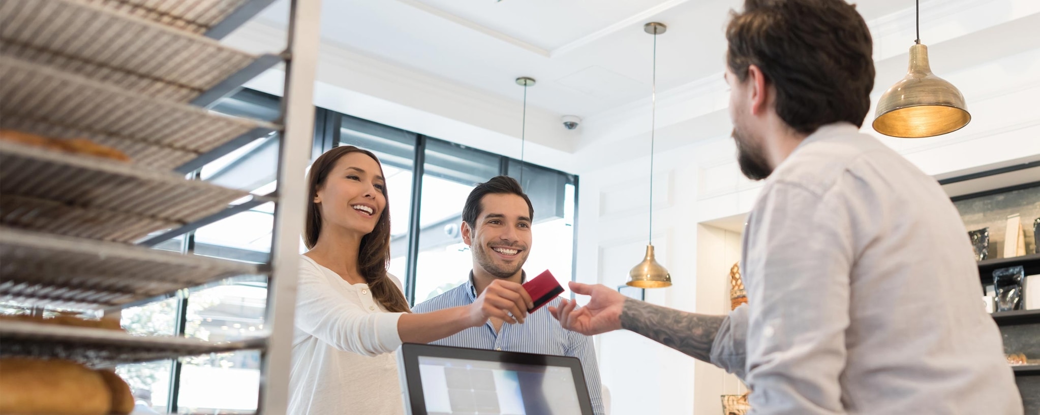 A couple happily handing the cashier their credit card at a modern-looking shop.