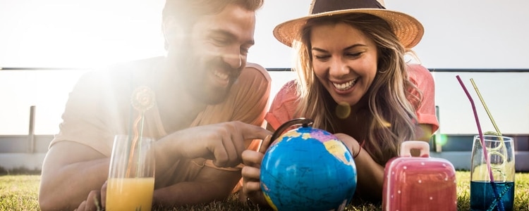 A couple points out destinations on a globe while planning their next trip over drinks on an outside terrace.