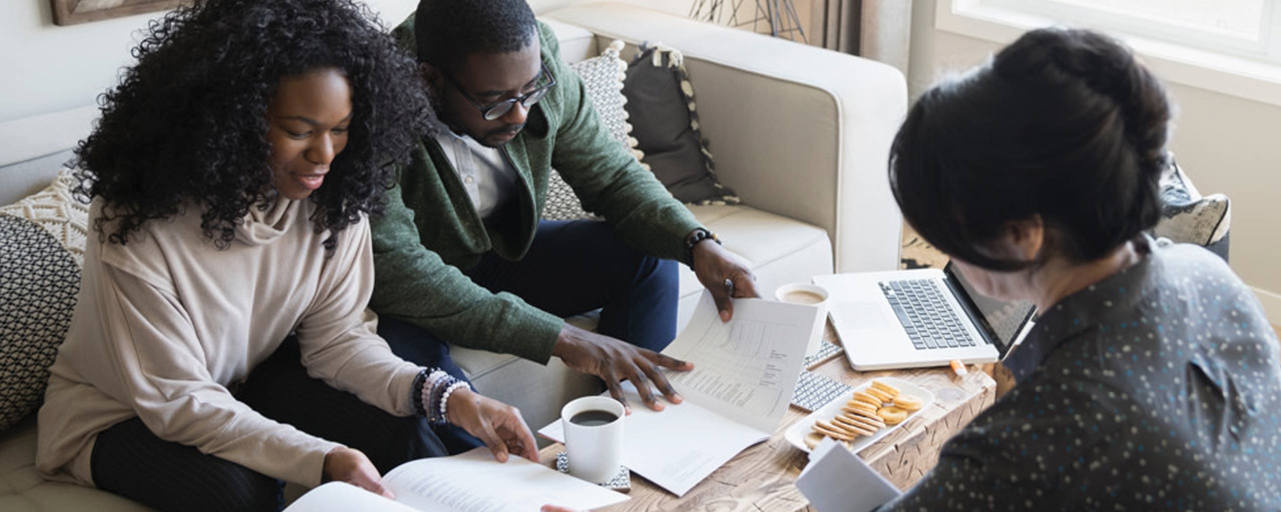 A couple looking over their bank account statements with their realtor at a coffee table while closing on their new house.