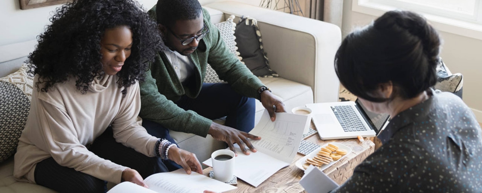 A couple looking over their bank account statements with their realtor at a coffee table while closing on their new house.