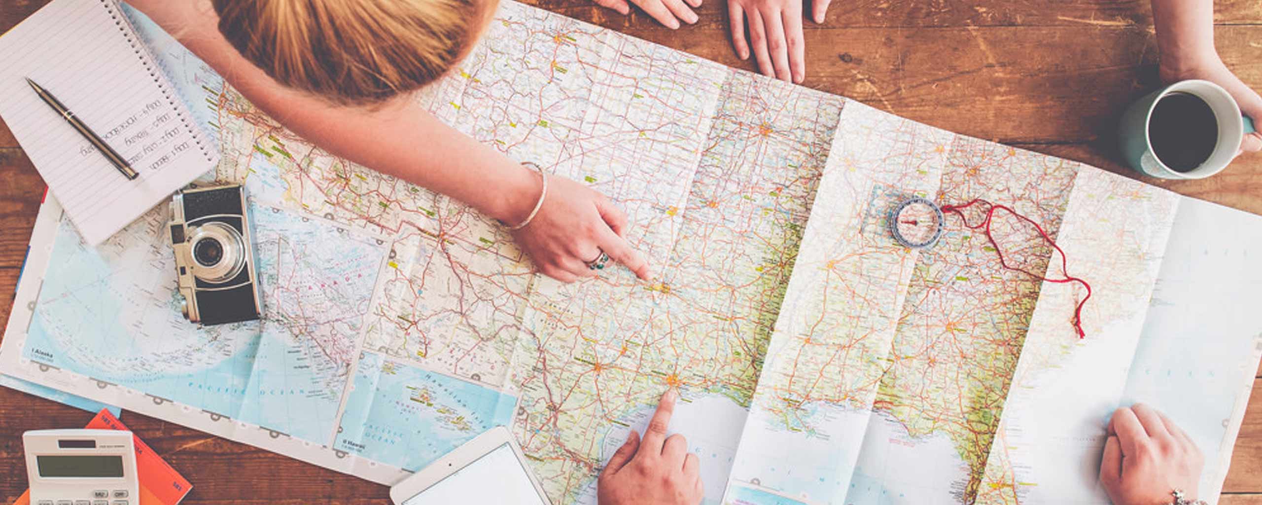 A group is shown from above as they point to a map to plan their next trip and figure out how to save money for travel.