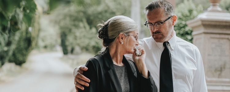 Man consoles grieving woman as she holds tissues near her face.
