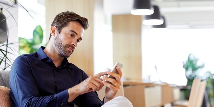Man, seated, taps his smartphone
