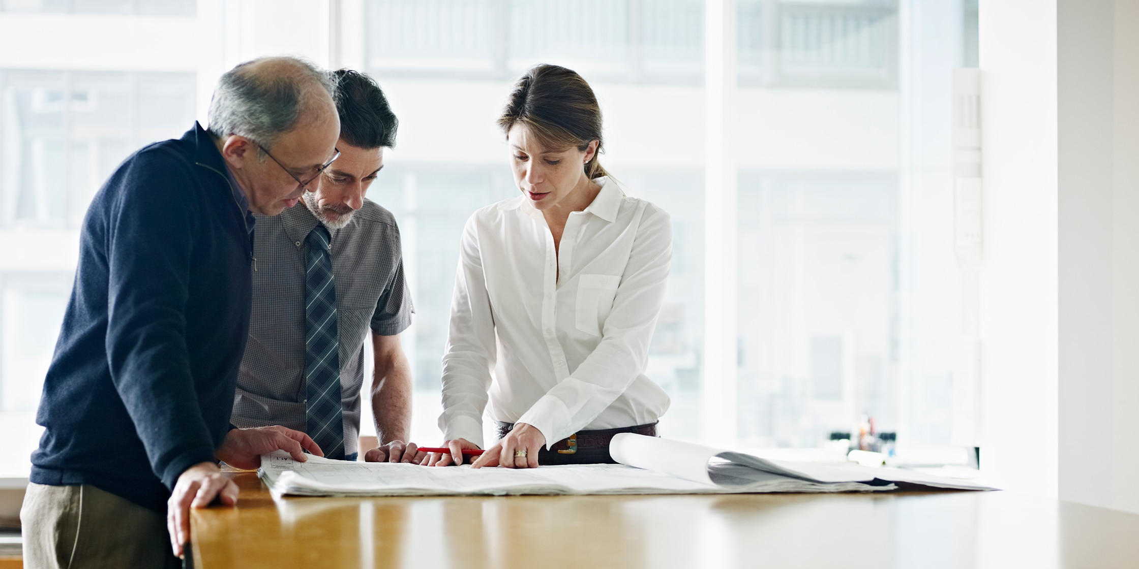 A woman and two men stand in an office, reviewing building plans