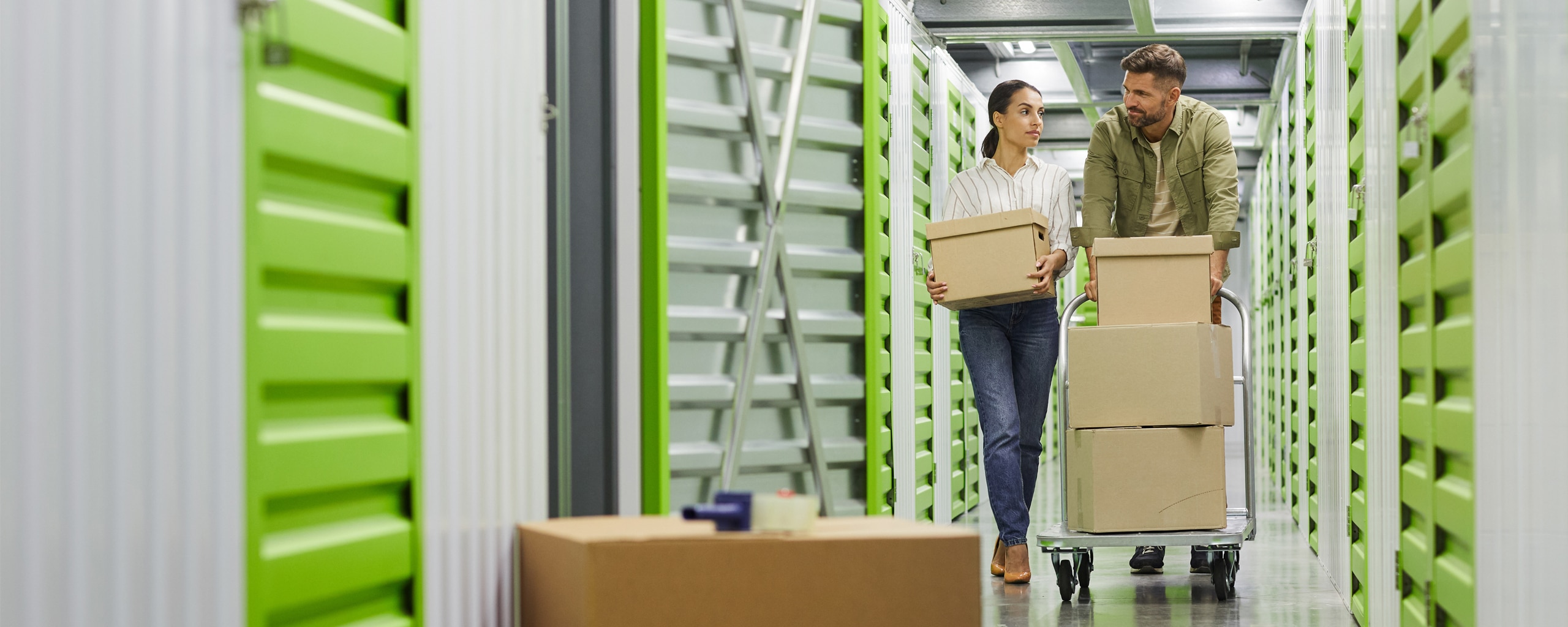 Two people walk through a storage facility with boxes.