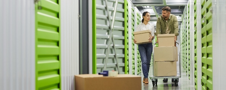 Two people walk through a storage facility with boxes.