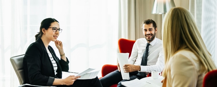 Three employees discuss business in an office setting.