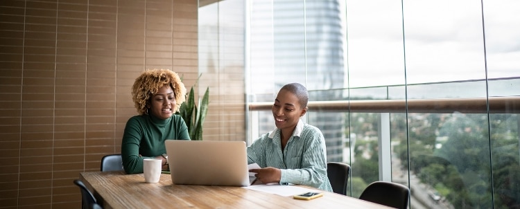 Two women sitting in front of a laptop in a conference room.
