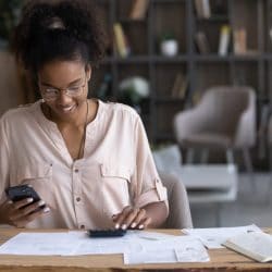 A smiling woman sits at a table and reviews her bills.