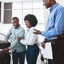 A couple looks at a car they want to lease as a salesman stands by them.
