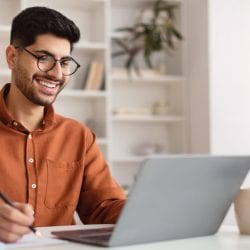 A smiling man with glasses studies his interest rates while sitting in front of his laptop.