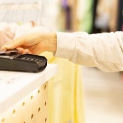 Hand taps credit card against pay terminal in clothing store.