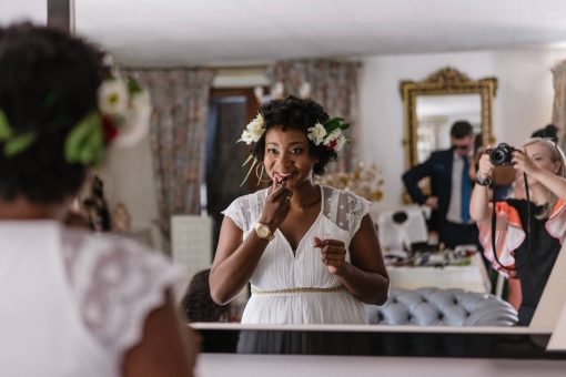 A woman in a white dress looks in a mirror and puts on lipstick.