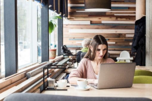 Woman sits at cafe table looking at laptop.