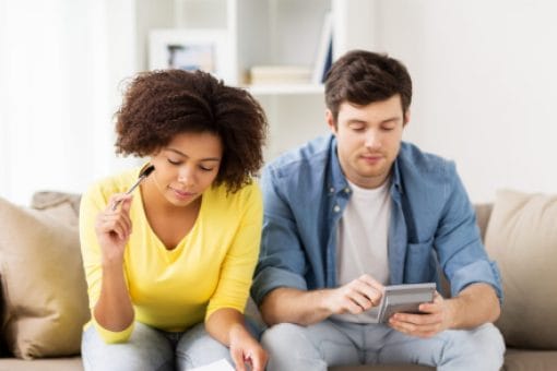 A couple sits on a couch reviewing papers and looking at a calculator.