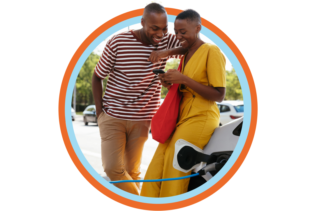 Young couple leans against car while it charges at an EV station