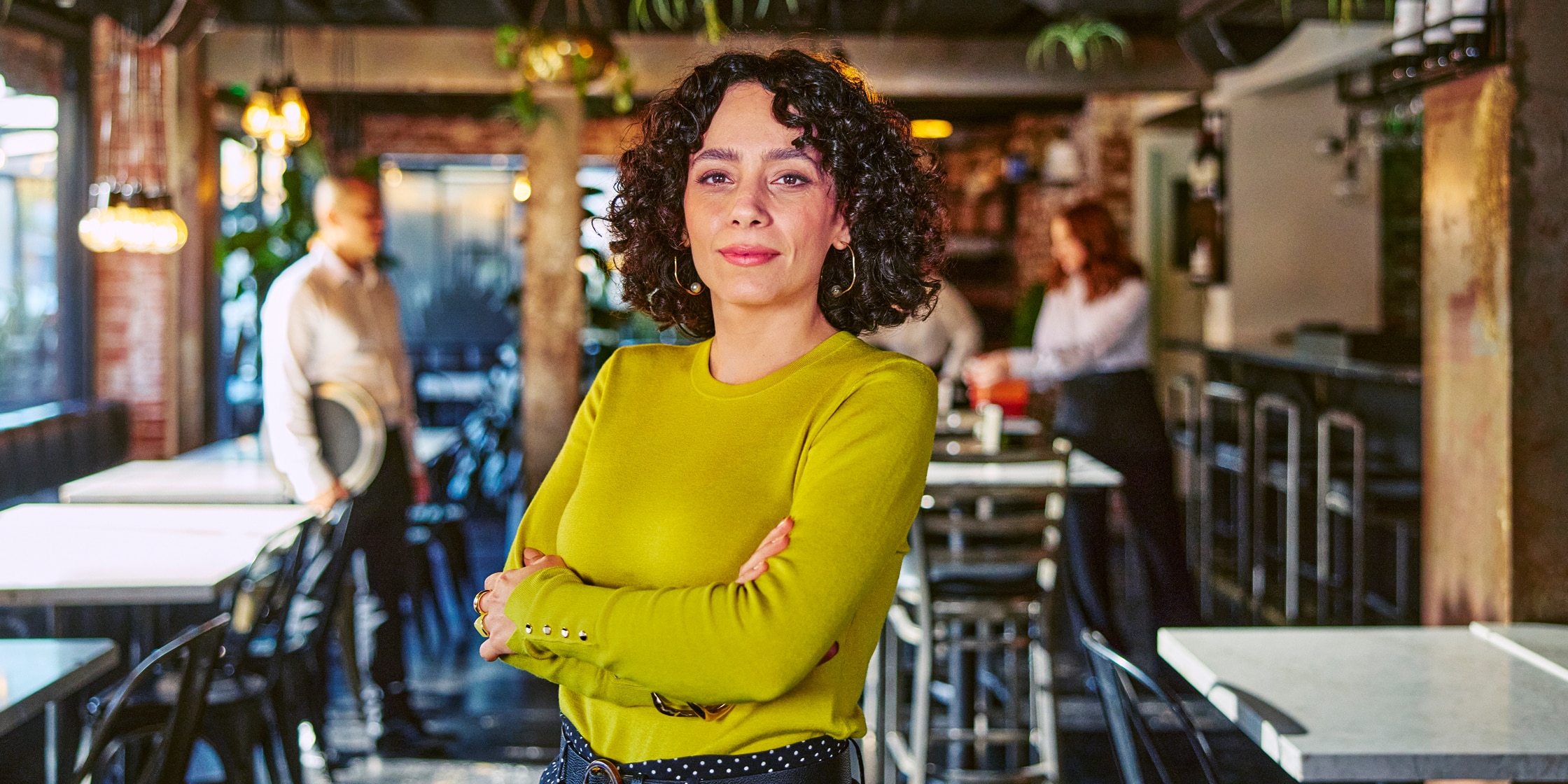 A woman in a bright green sweater stands with her arms crossed.