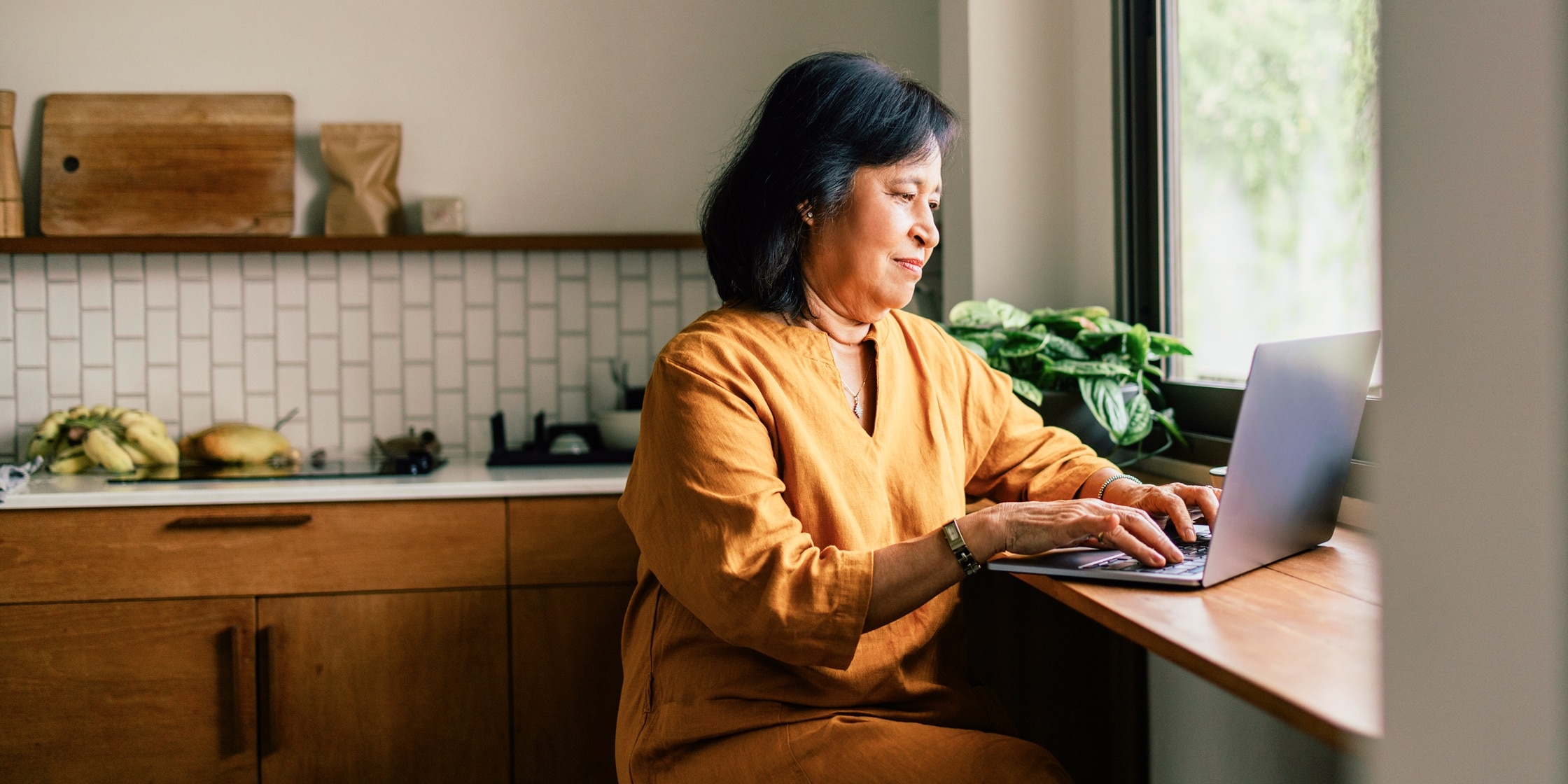 A woman types on her laptop while seated at her kitchen counter.