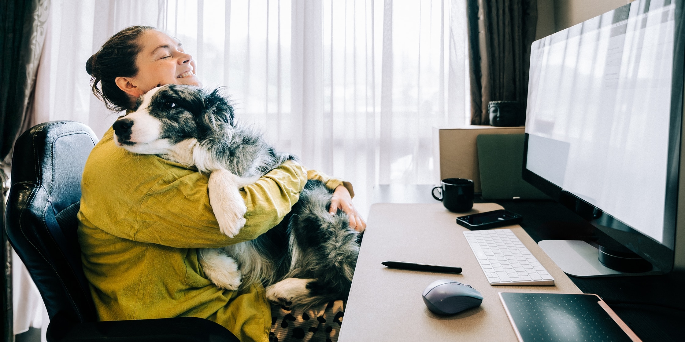 A woman hugs her dog in her lap while she works at her home office.