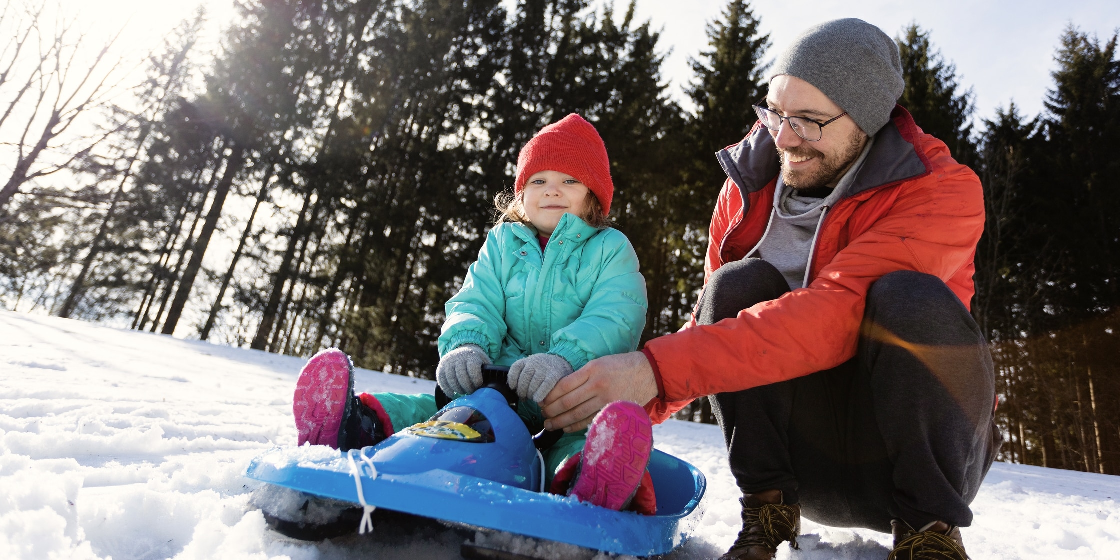 A father helps his young daughter navigate a child’s sled in the winter snow.
