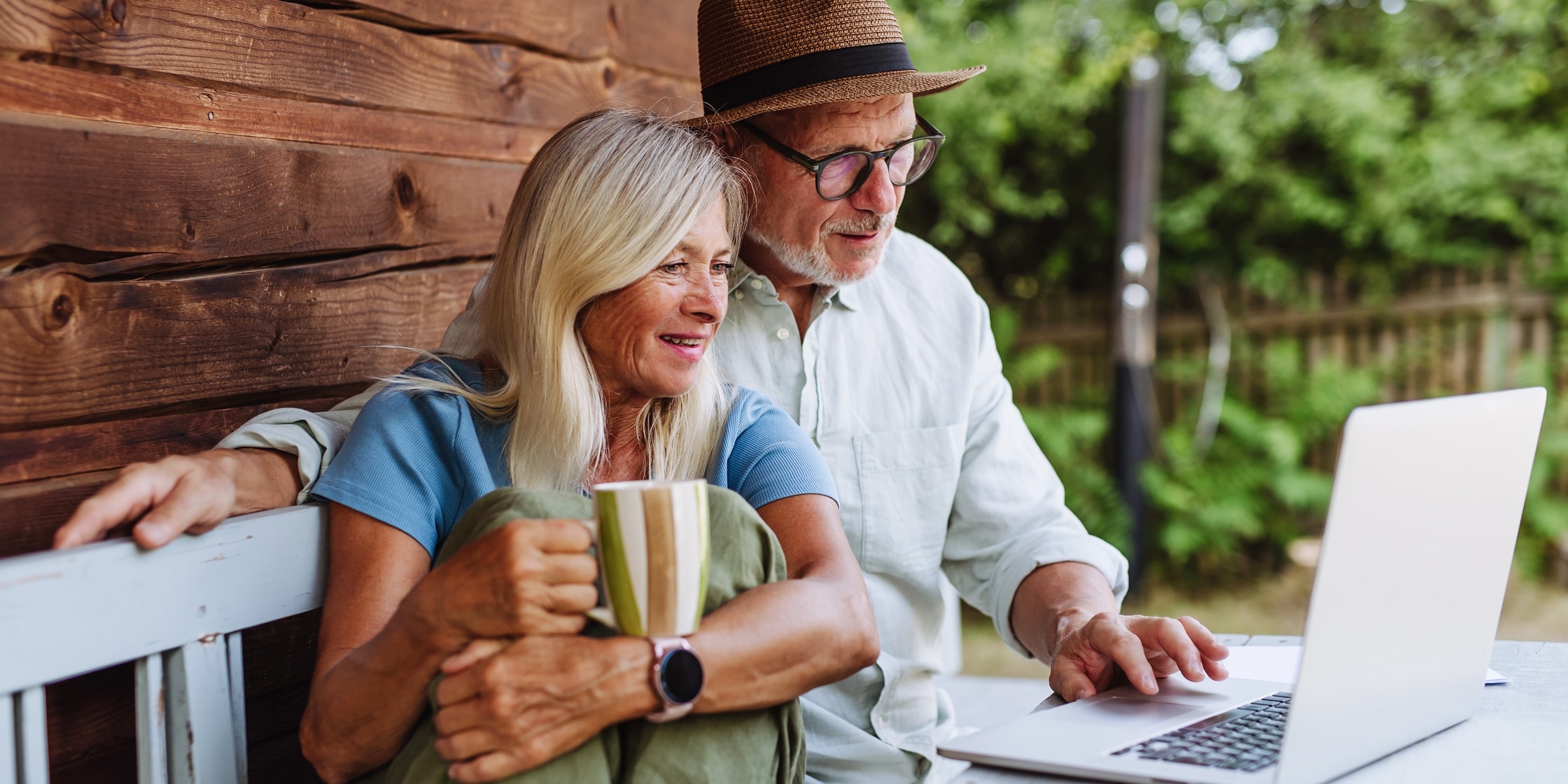 A senior couple sits on their porch and looks at their laptop.