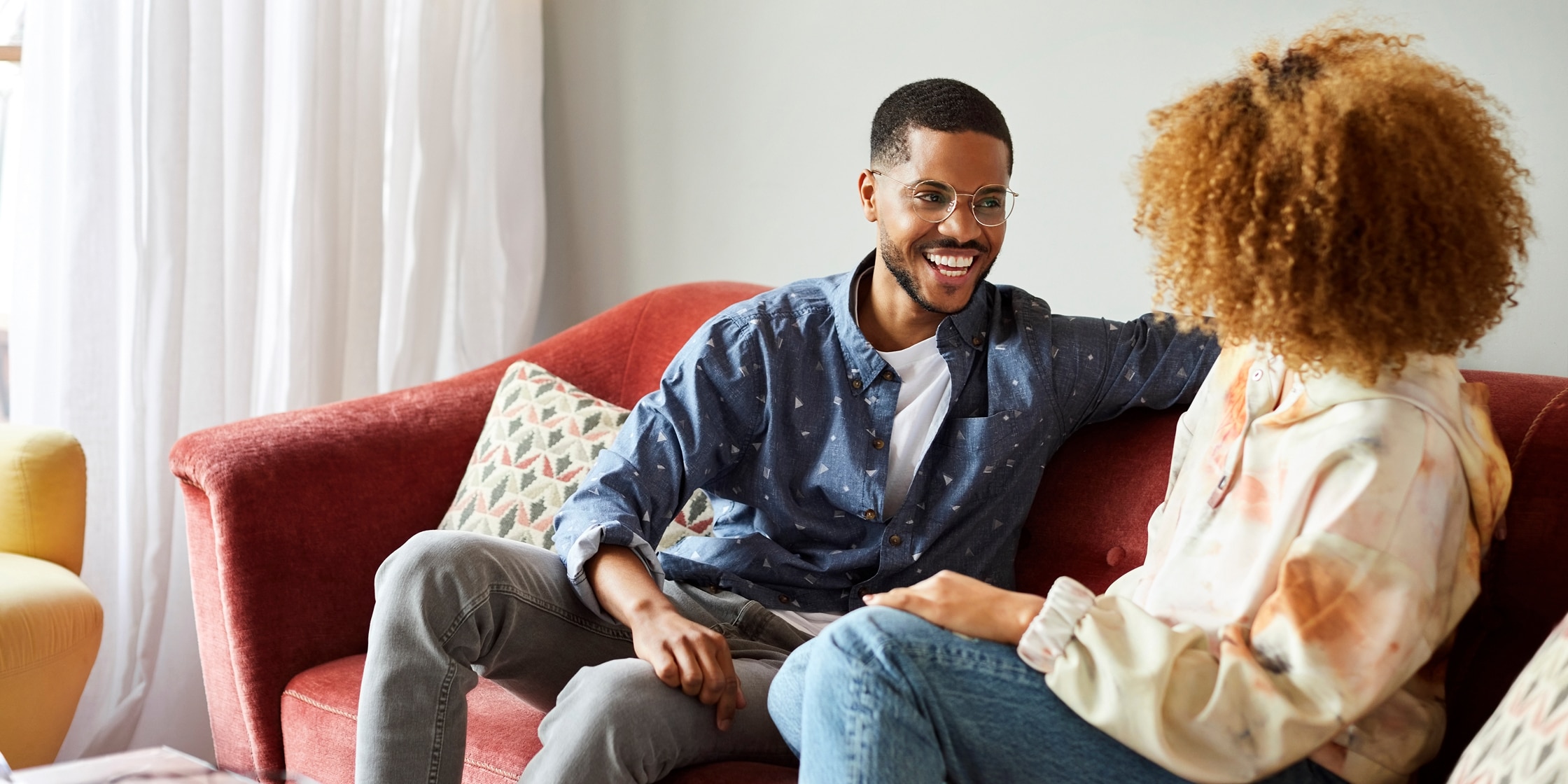 A smiling young couple chats on their living room couch.
