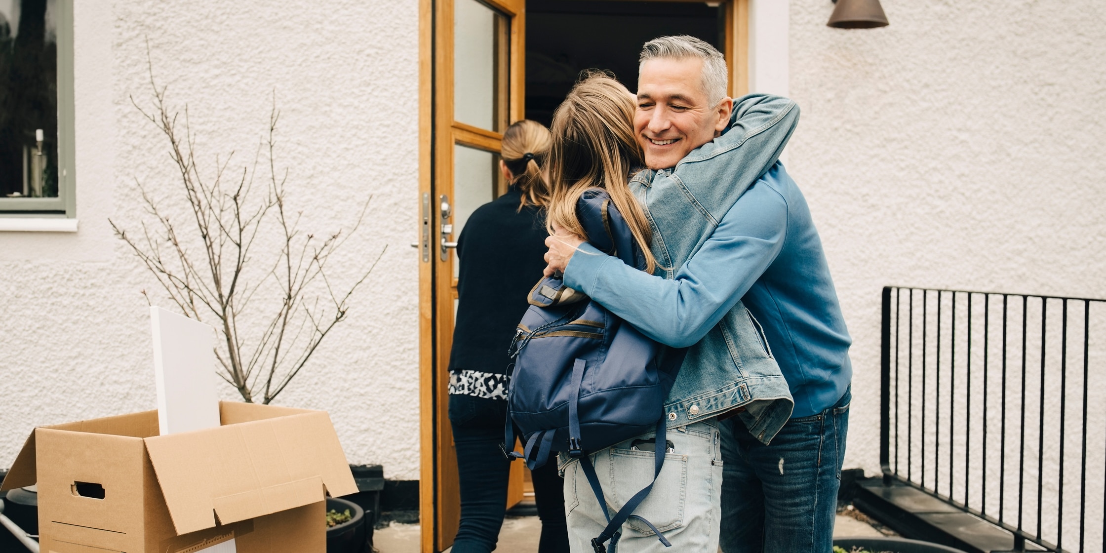 A man and his daughter embrace in front of a doorway with moving boxes out to the side.
