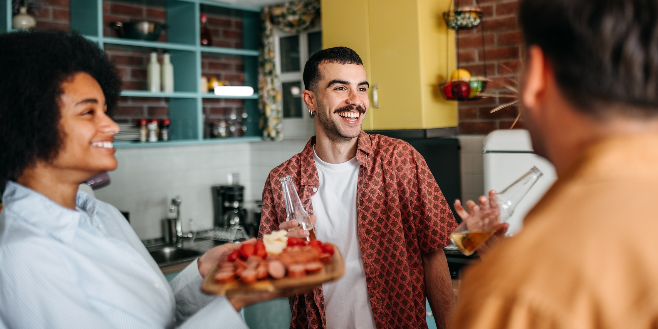 Three friends enjoy beverages and snacks in a home kitchen.