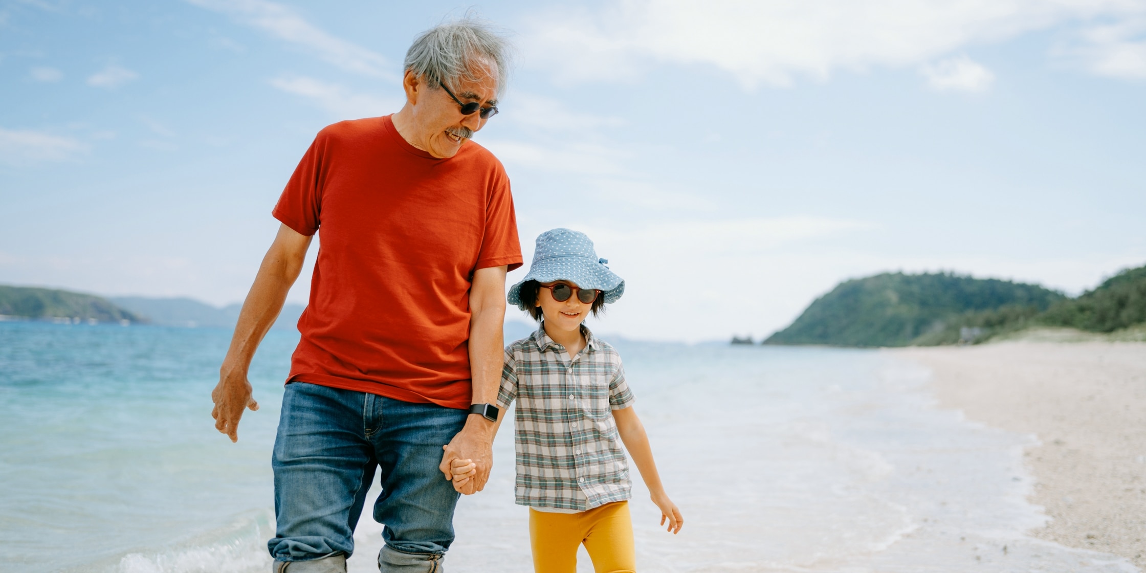 A grandfather and his young grandson walk in the beach surf.
