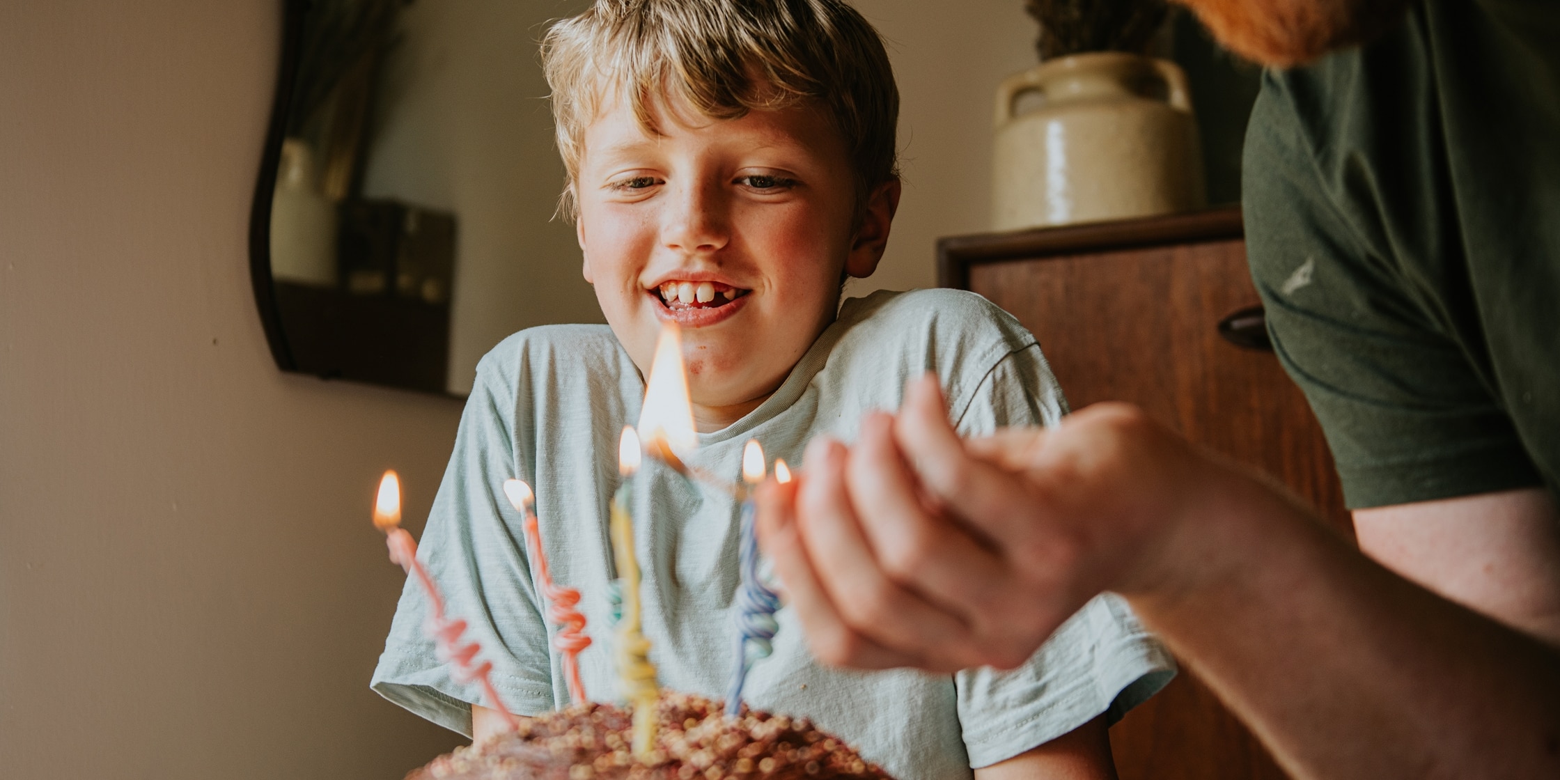 A smiling boy leans over his birthday cake as his father lights the candles.