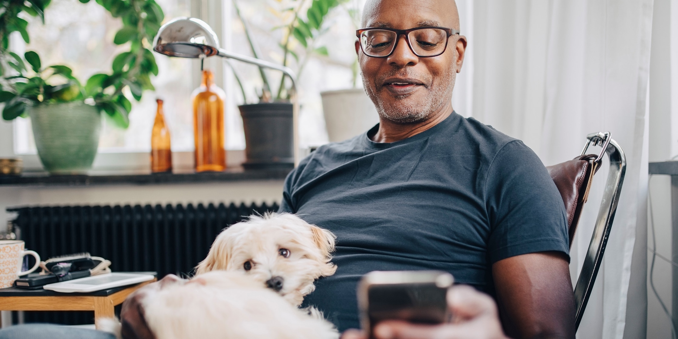 A man checks his phone while his dog sits in his lap.