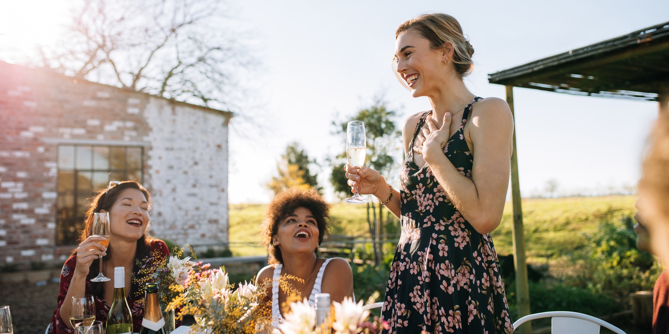 A woman holding a champagne glass smiles earnestly while standing in front of her friends at a bridal shower.