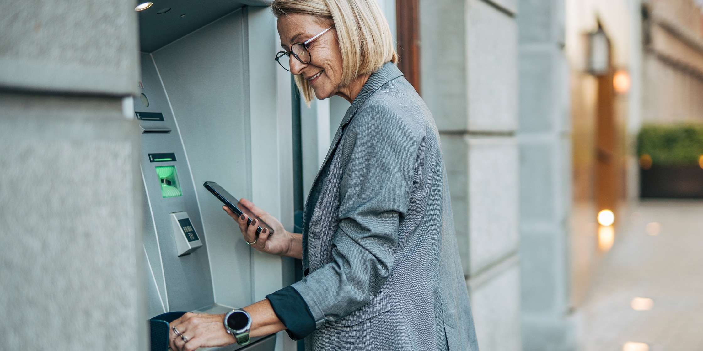 A smiling woman withdraws money at an ATM.