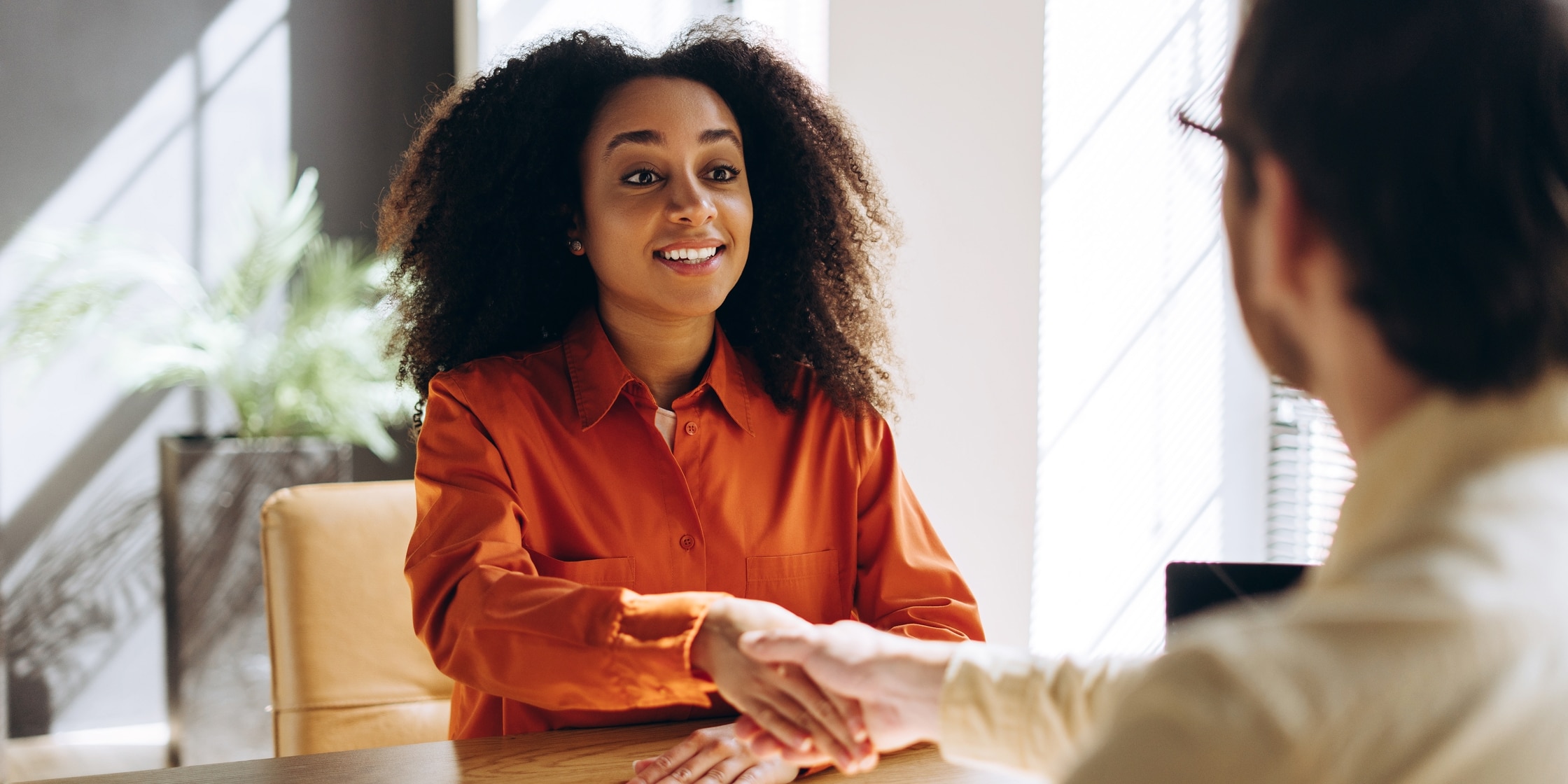 A woman and man shake hands across a table.