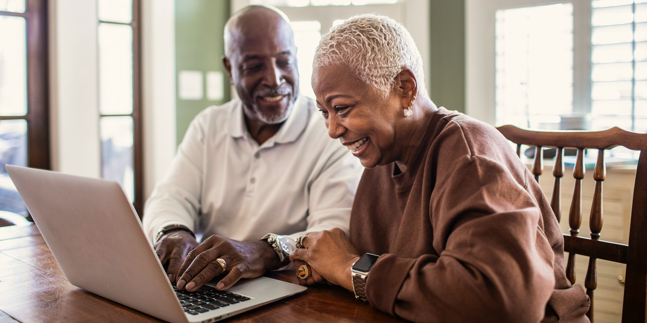 A senior couple laughs together in front of their laptop.