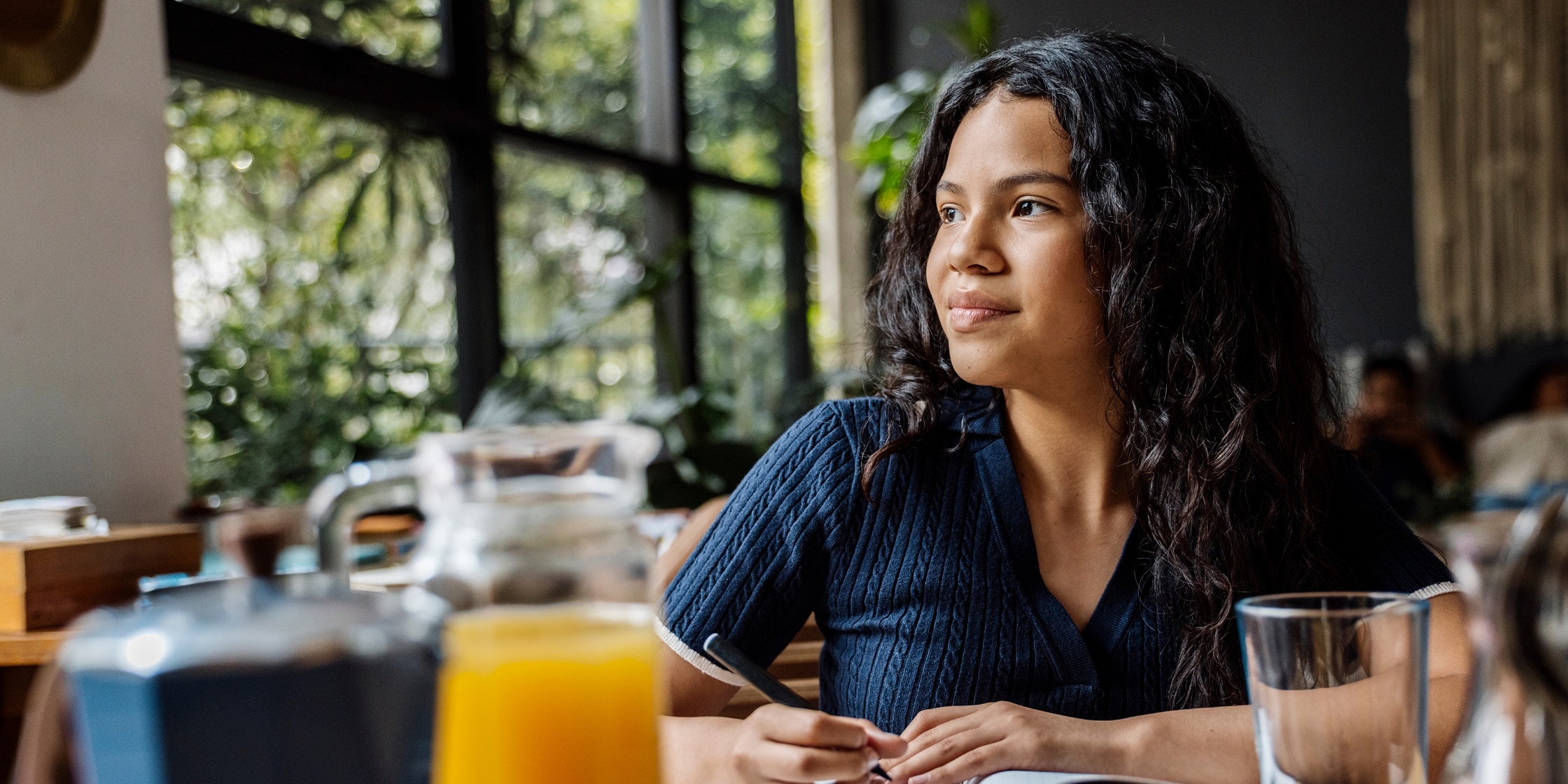 A young woman sits at a breakfast counter and writes in her notebook.