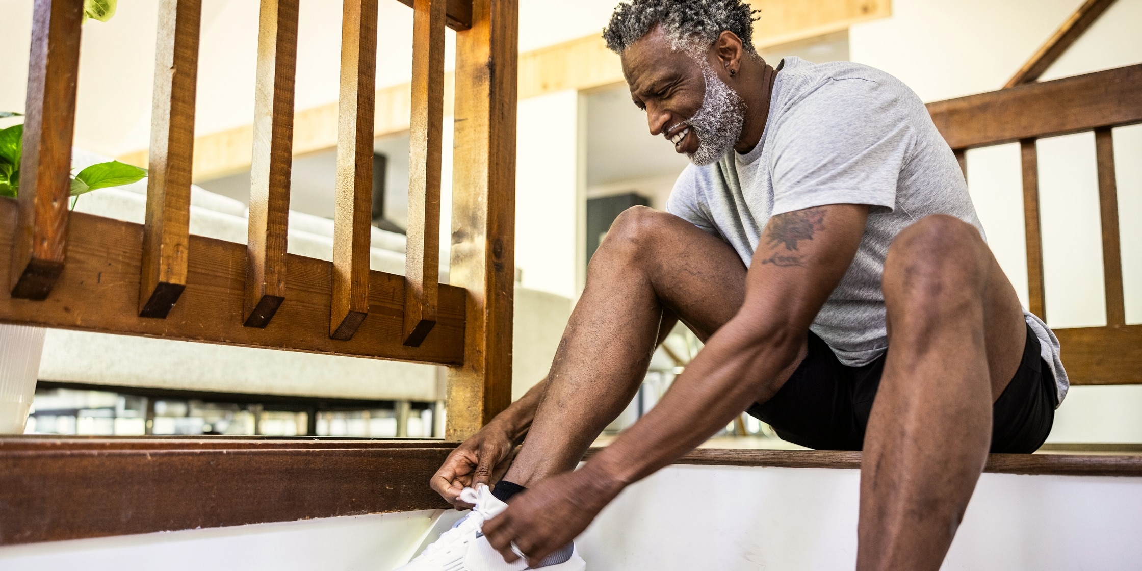 A man ties his running shoes while perched at the top of his staircase.