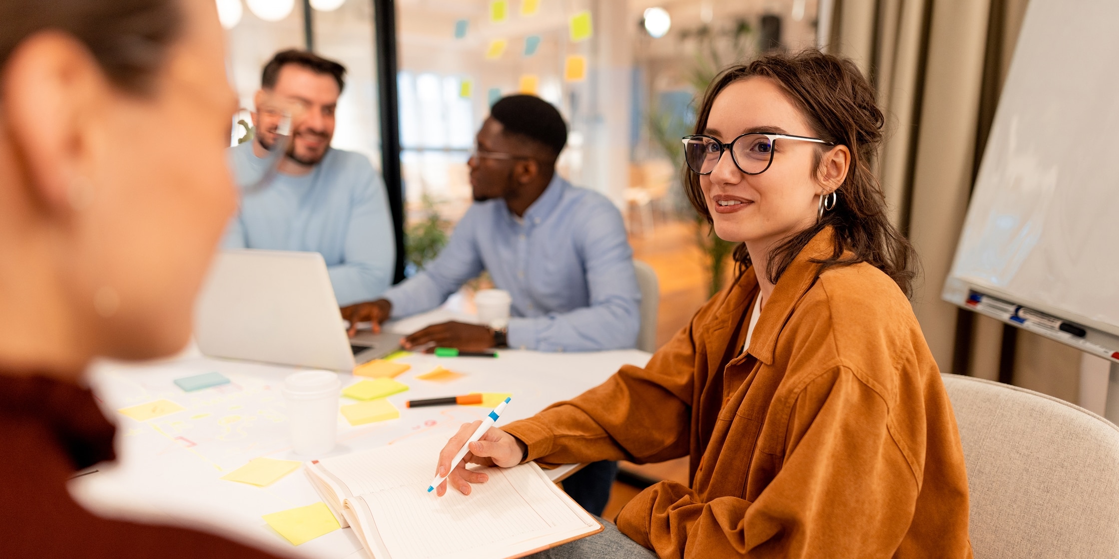 Four young office employees sit around a conference table strewn with post-its.