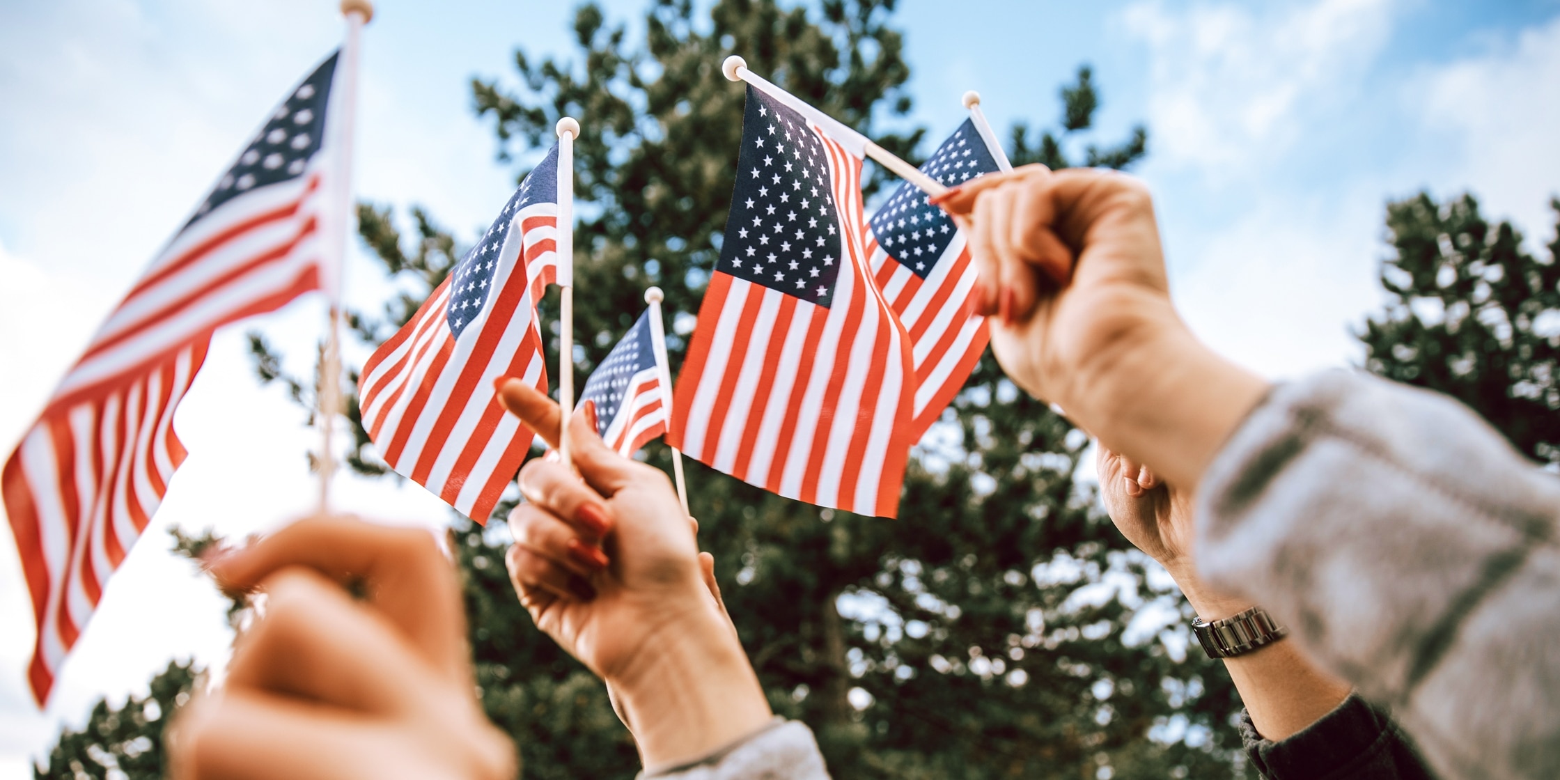 A group of 4th of July celebrators wave tiny American flags in the air.