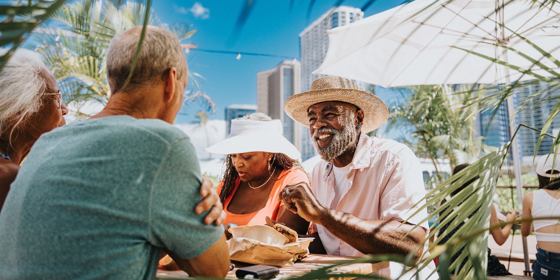 Two senior couples sit at a rooftop patio table conversing against the backdrop of cityscape.